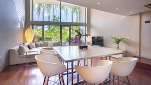 A modern living room with a large dining table, white chairs, a sofa, and a TV. - Petitenget 501 (Keroboken Kelod)