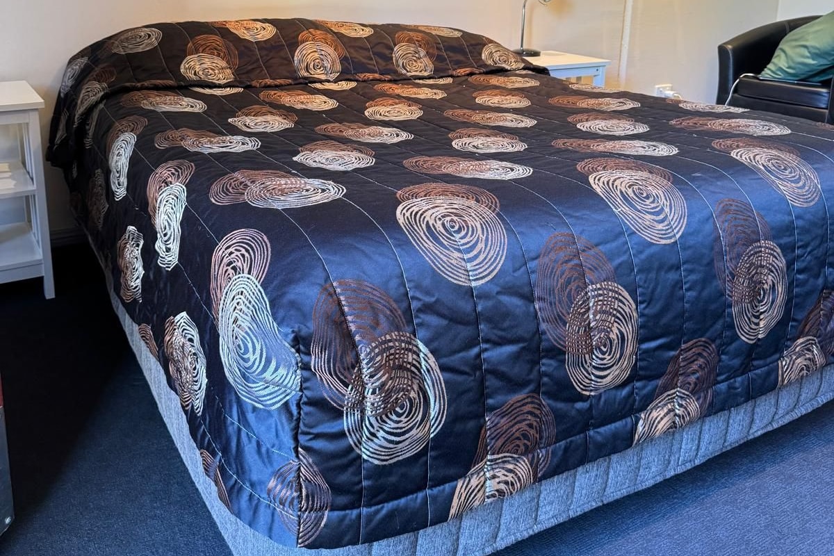 A neatly made bed with a patterned duvet, a bedside table with a lamp, and a framed picture on the wall.