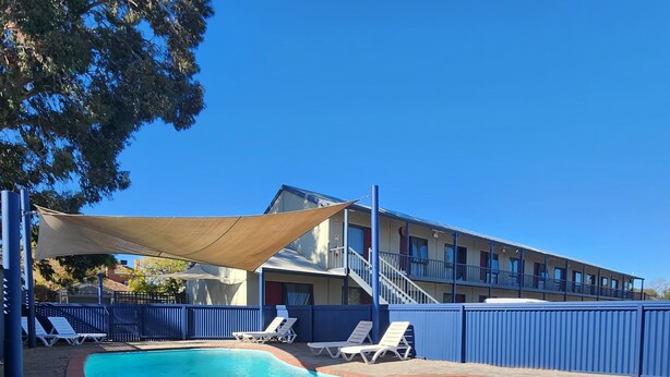 A swimming pool with a brick border, surrounded by lounge chairs and a shaded area. - Wentworth Central Motor Inn (Wentworth)