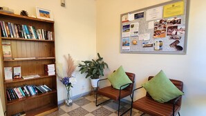 A reception area with a wooden bookshelf, two chairs with green cushions, a bulletin board with various notices, and a potted plant. - Wentworth Central Motor Inn (Wentworth)