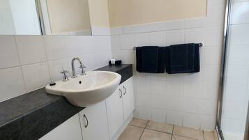 A bathroom with a white sink, dark countertop, white cabinets, and a tiled floor.
