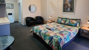 A bedroom with a bed, two chairs, a desk, a mirror, a ceiling fan, a painting, and a small table with a lamp. - Wentworth Central Motor Inn (Wentworth)