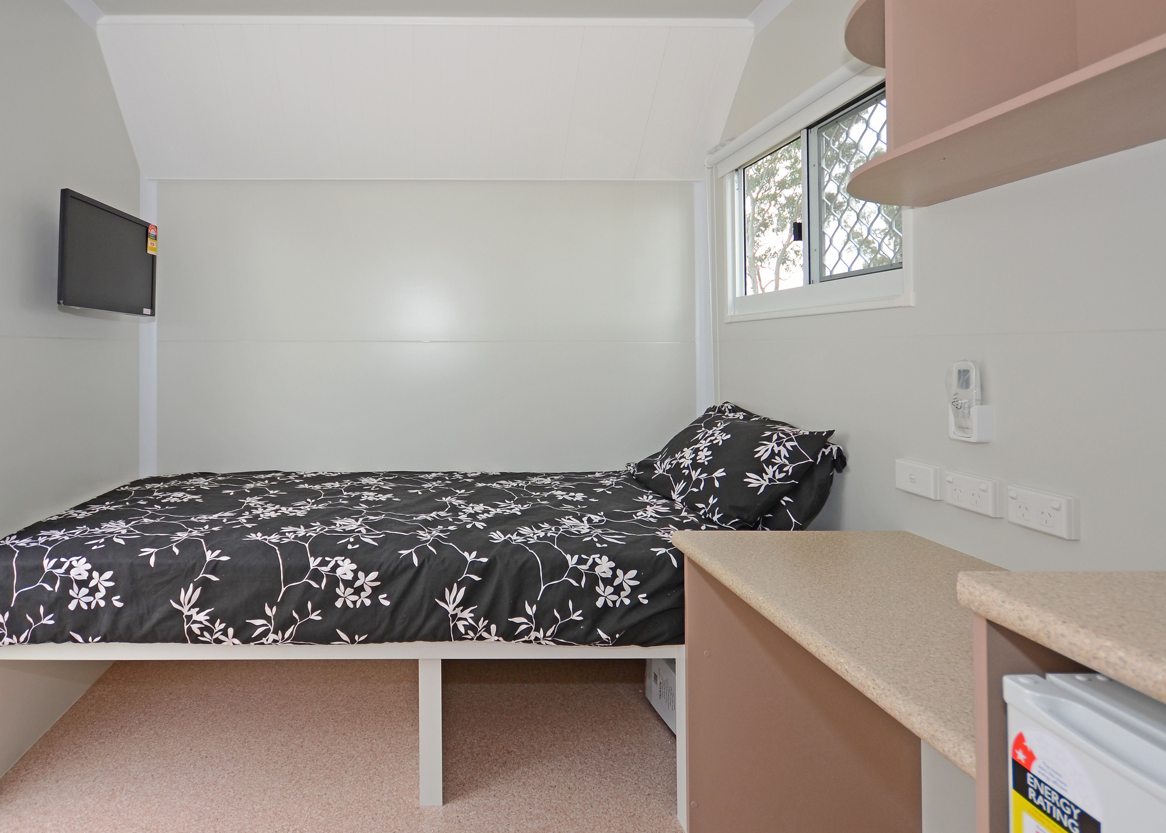 Une chambre avec un lit, un téléviseur fixé au mur, une fenêtre donnant sur un beau paysage et une prise électrique sur le mur.