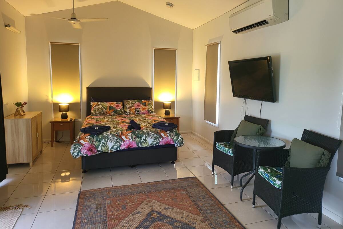 A bedroom with a bed, bedside lamps, a TV, a small table, and a chair.