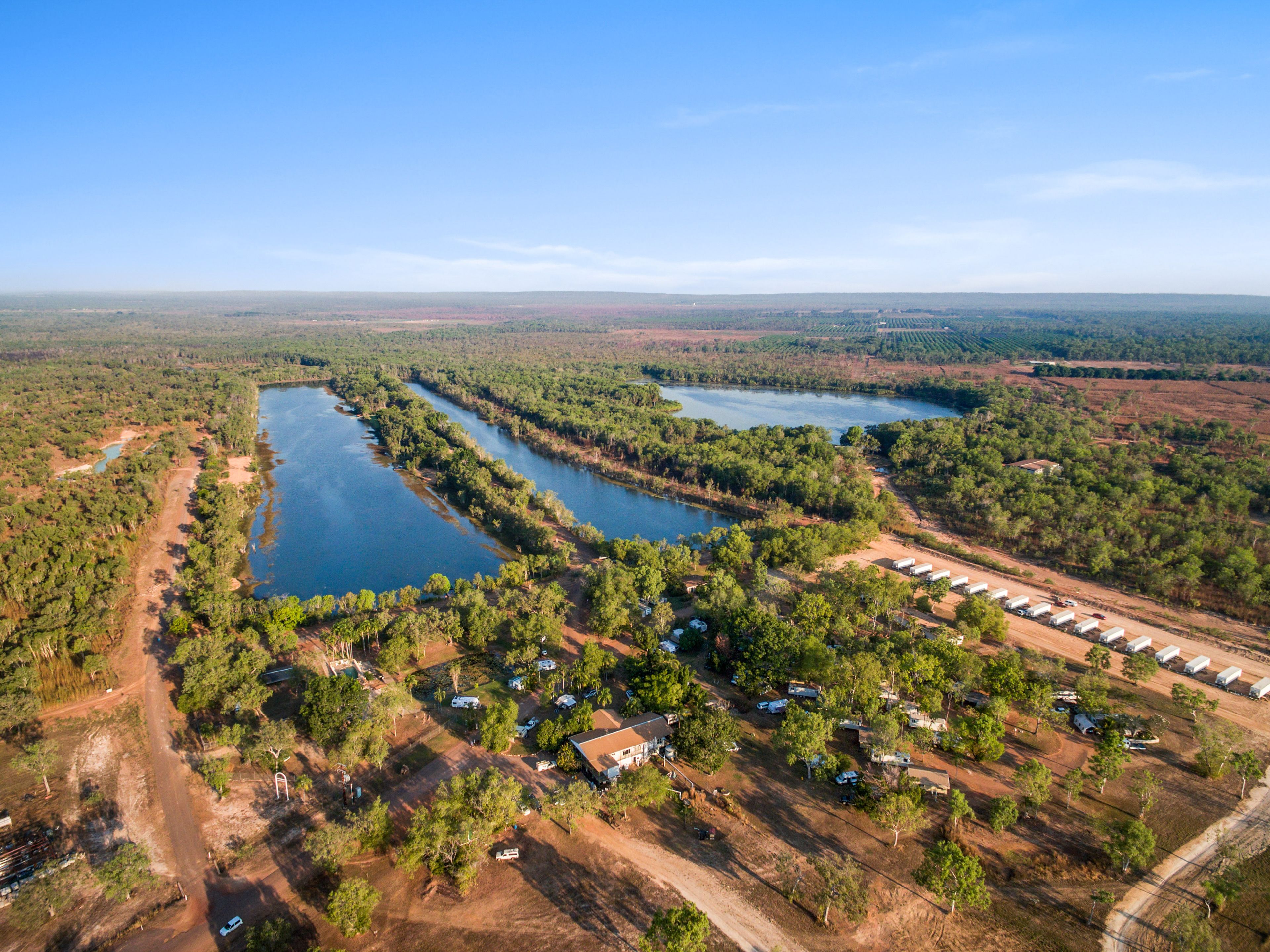 Vue aérienne d’un terrain de camping comprenant plusieurs cabanes, un lac et la forêt environnante.