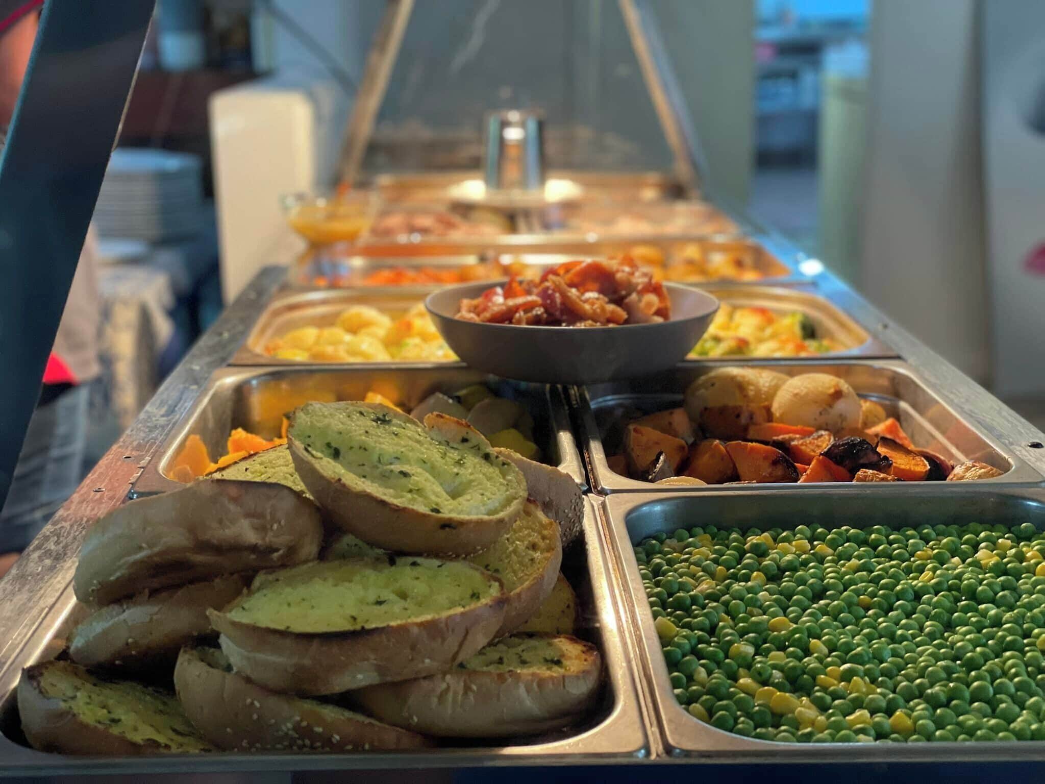 Een buffet met diverse gerechtjes, zoals sneetjes brood, geroosterde groenten en een schaal met doperwten.