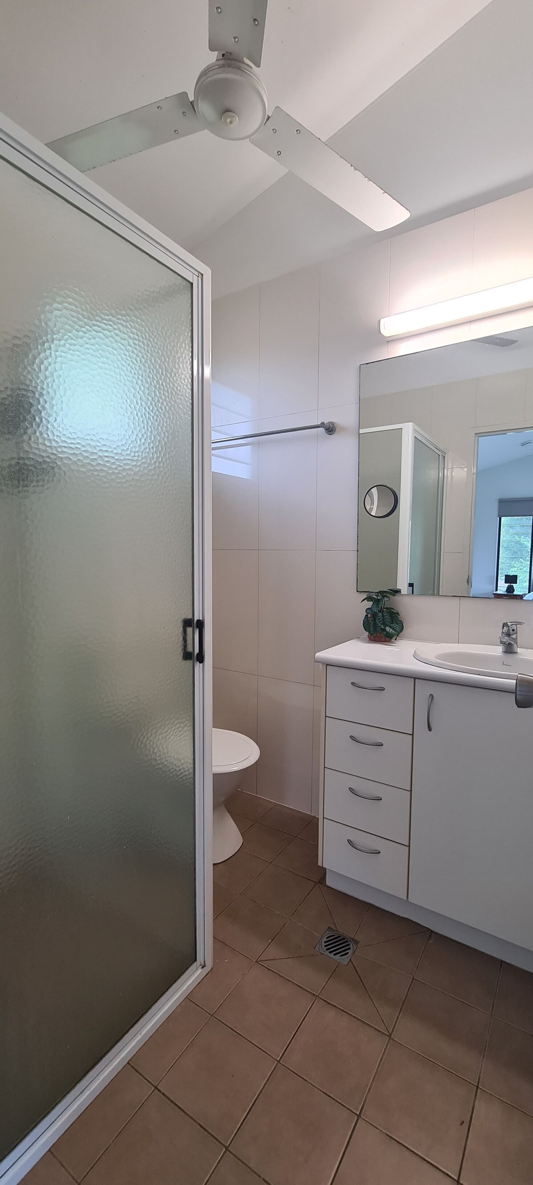 Un bagno con un water, un lavandino, uno specchio e una ventola a soffitto.