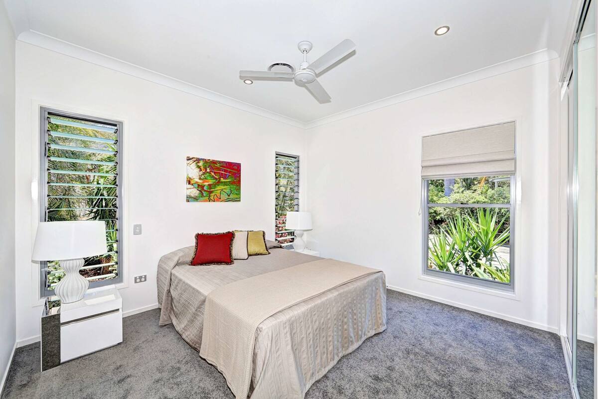 Une chambre à coucher comprenant un lit, deux tables de chevet, un ventilateur de plafond et une fenêtre donnant sur un paysage verdoyant.