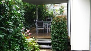 A covered patio area with a table and chairs, surrounded by lush greenery and a wooden deck. - Woodgate Beach Houses (Woodgate)