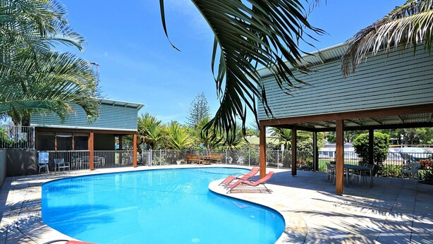 A swimming pool with lounge chairs, a covered seating area, and surrounding palm trees. - Woodgate Beach Houses (Woodgate)