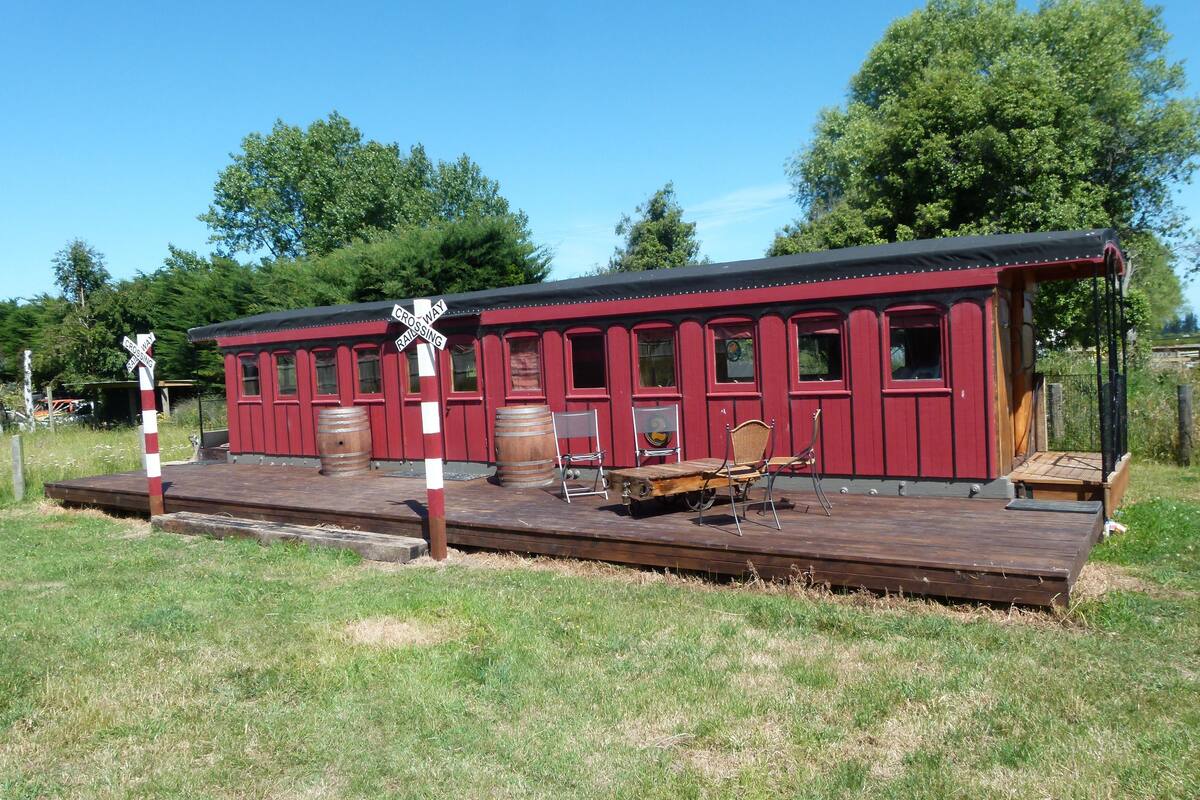 A red train station platform with a wooden bench and a chair.