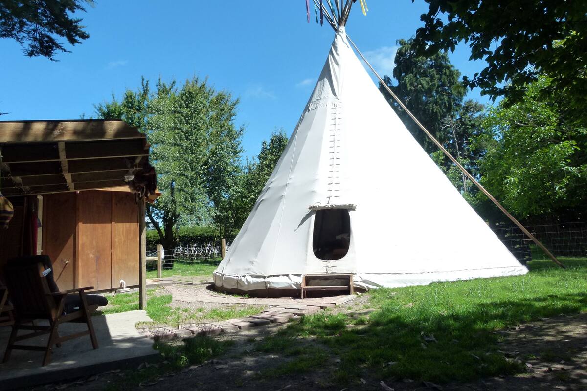 A white teepee with a small entrance and a wooden structure to its left.