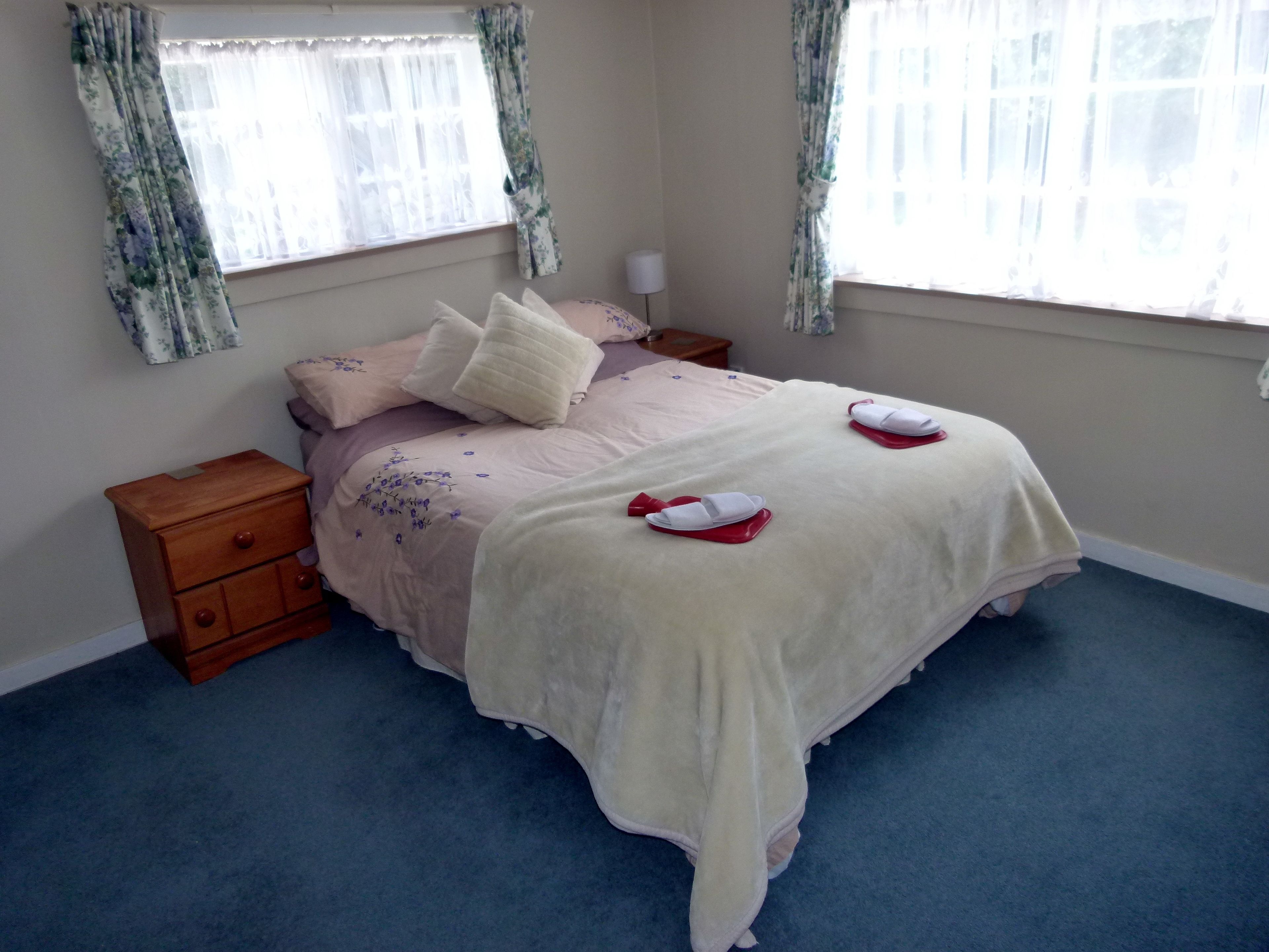 Un dormitorio con una cama, dos mesitas de noche, un aparador de madera y una ventana con cortinas florales.