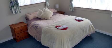 Un dormitorio con una cama, dos mesitas de noche, un aparador de madera y una ventana con cortinas florales.
