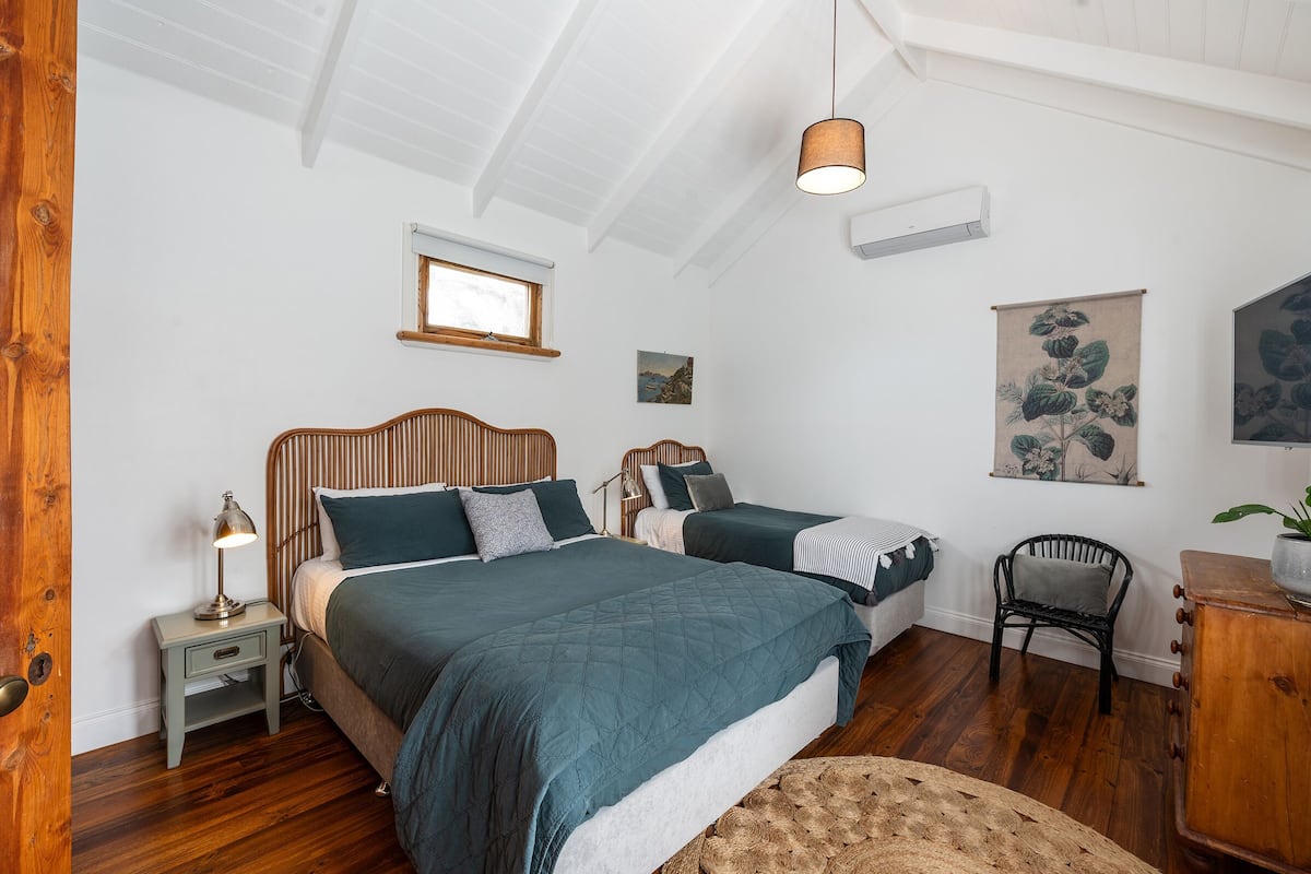 A bedroom with two beds, a nightstand with a lamp, a wooden chair, and a small table with a plant.