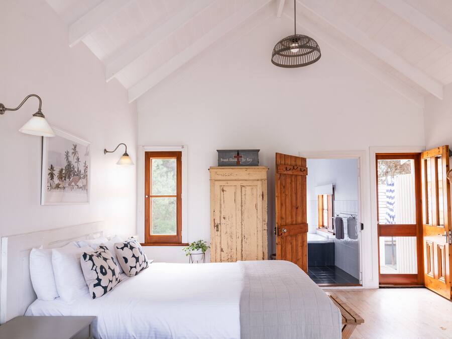A bedroom with a large bed, a wooden wardrobe, a small table, and a door leading to a bathroom.