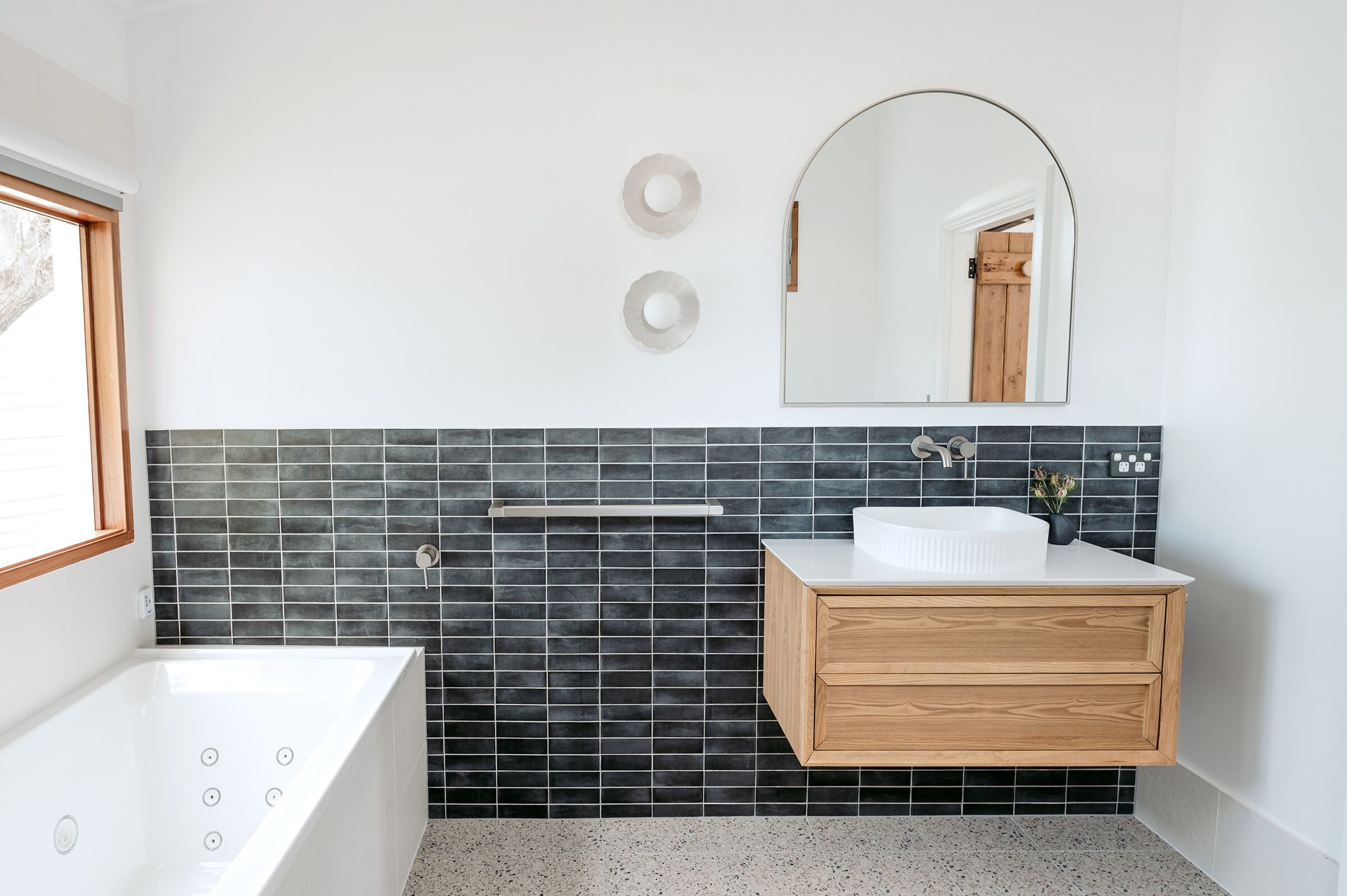 Een moderne badkamer met een vrijstaand bad, een houten wastafelmeubel met een witte wastafel en een grote spiegel erboven.