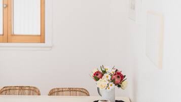 Un coin repas avec une table blanche, des chaises en osier, une horloge et un vase de fleurs.