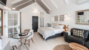 Quarto moderno com uma cama, sofá de couro preto, mesa de jantar com cadeiras e um espelho grande.