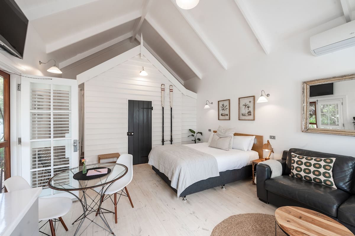 A modern bedroom with a bed, a black leather sofa, a dining table with chairs, and a large mirror.