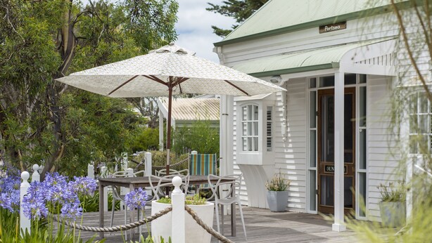 Um deck de madeira com área de estar externa, um guarda-sol branco e um edifício com a placa 'Portsea'.