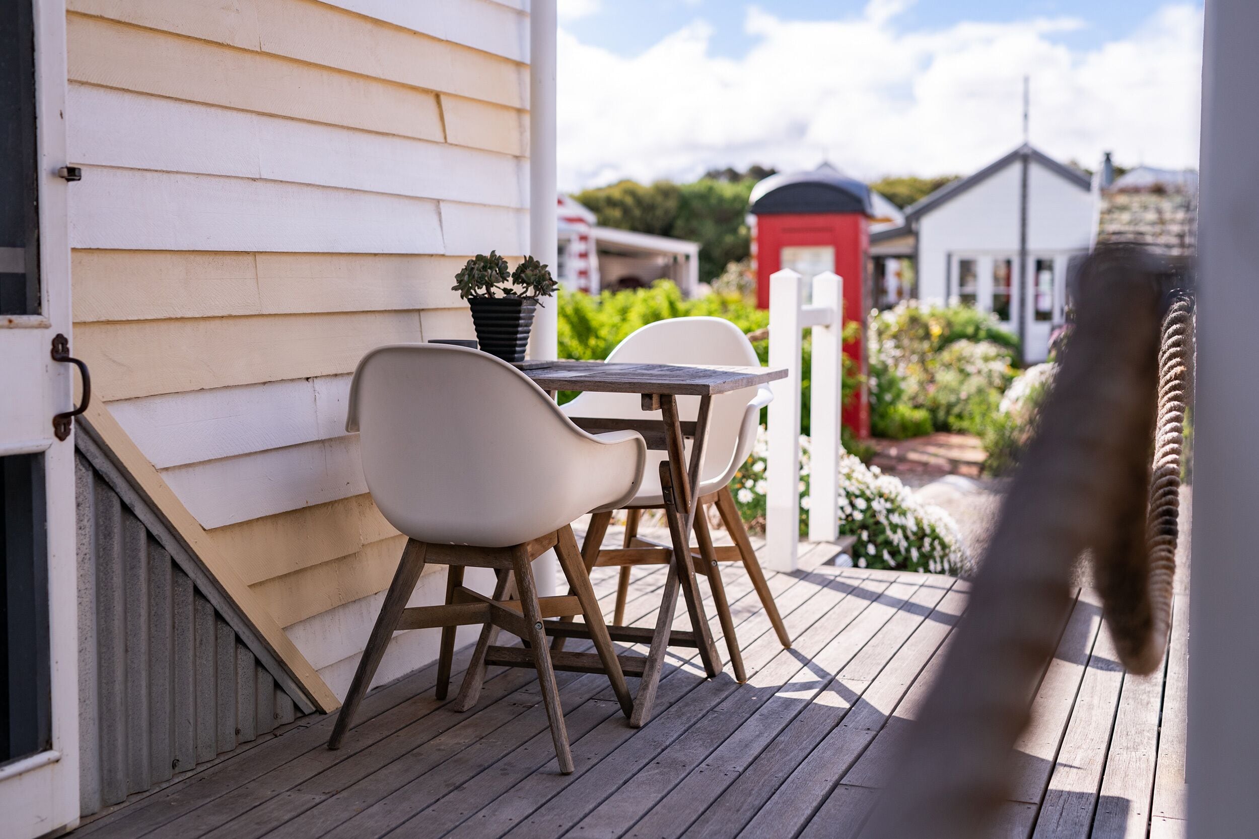 A wooden deck with a table and chairs, a potted plant, and a red mailbox in the background.