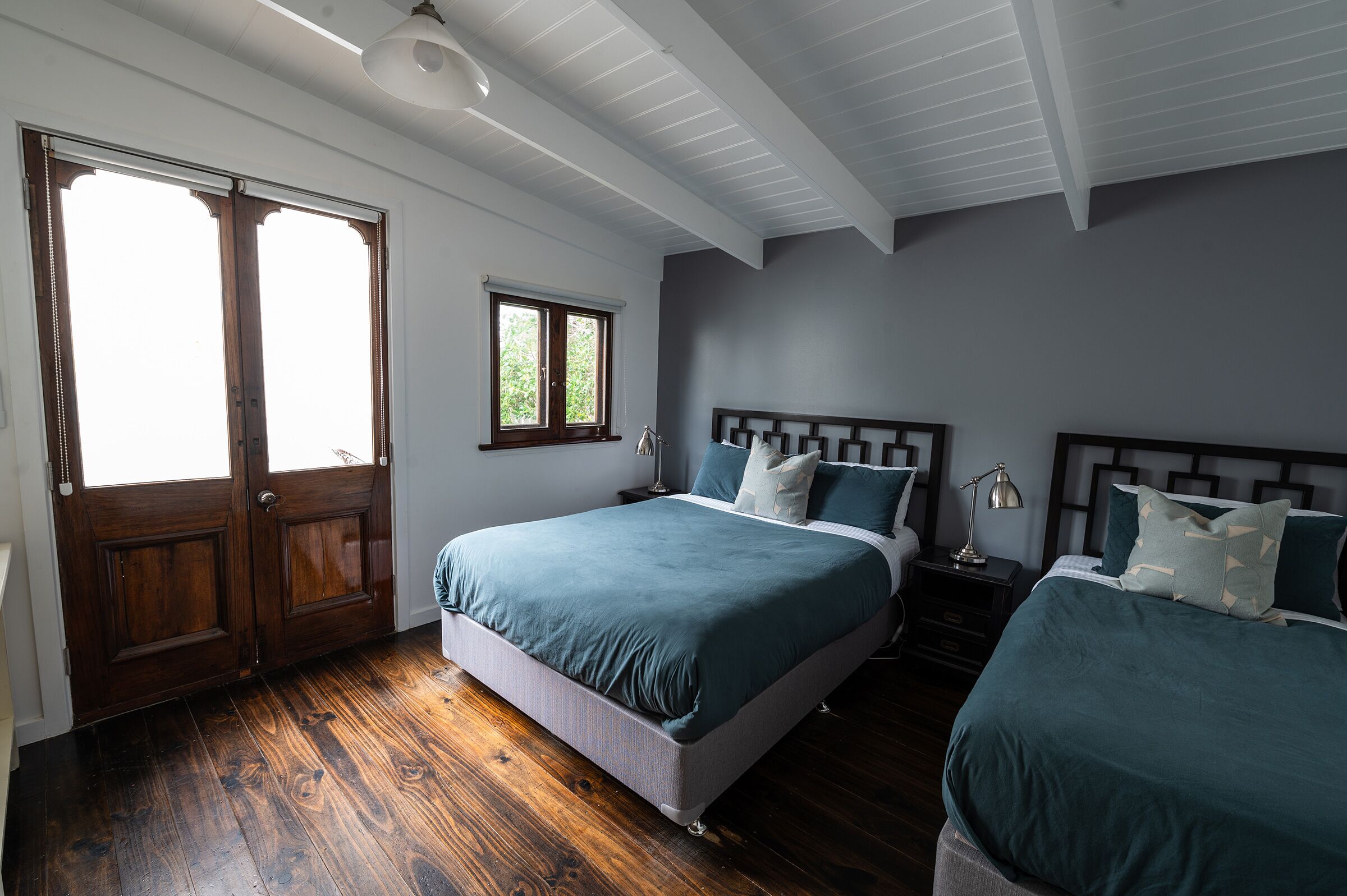 A bedroom with two beds, wooden flooring, a window, and a door.