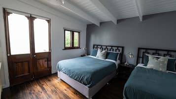Een slaapkamer met twee bedden, houten vloeren, een raam en een deur.