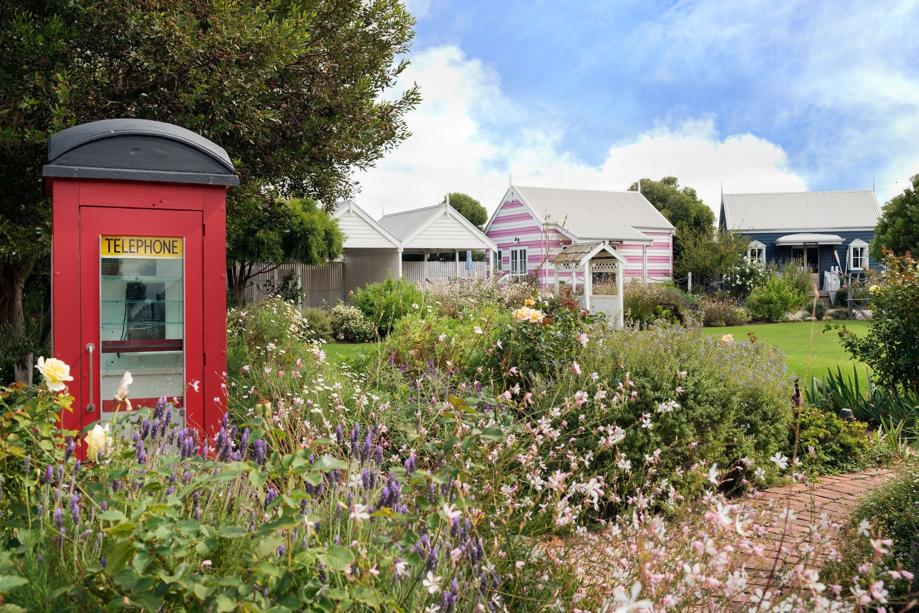 A traditional red telephone booth and a row of quaint, colorful houses with a well-maintained garden in the foreground.