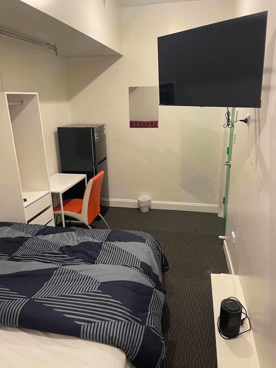 Una habitación de hotel con cama, escritorio, silla, televisor y cubo de basura.