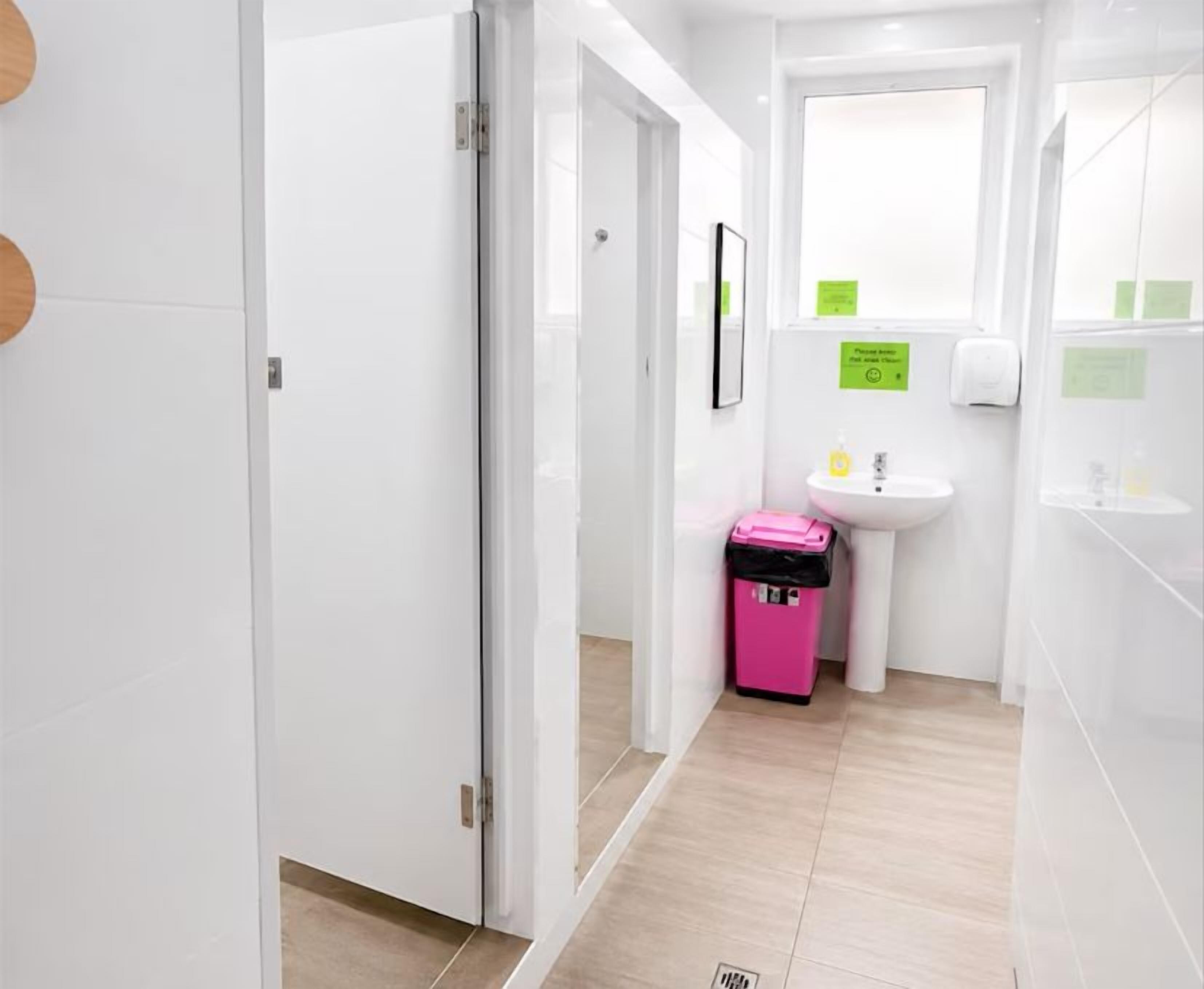 A clean, modern bathroom with a white sink, a mirror, and a pink trash bin.
