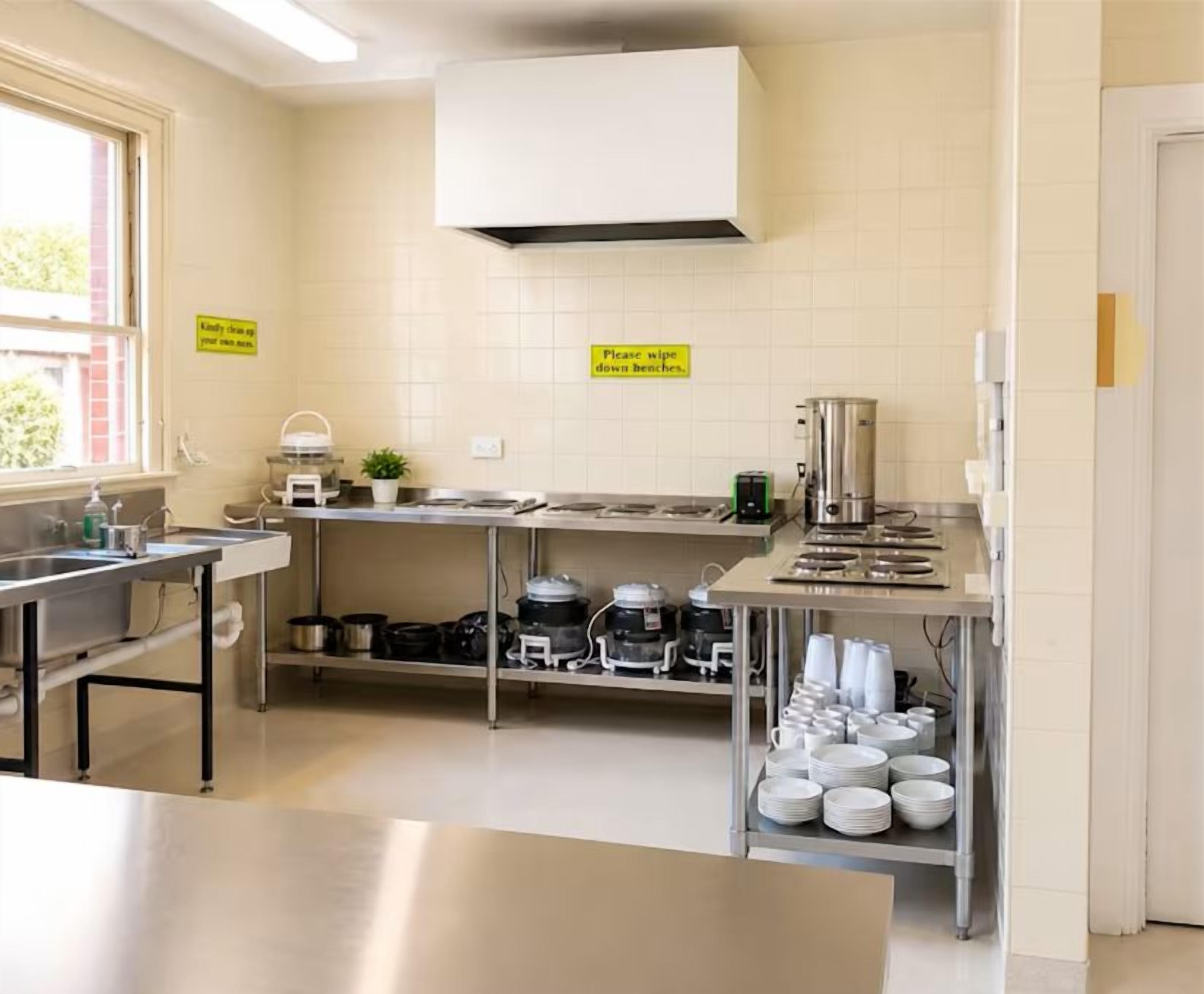A kitchen with stainless steel appliances, a sink, and a stove. There are signs on the wall and a shelf with dishes.