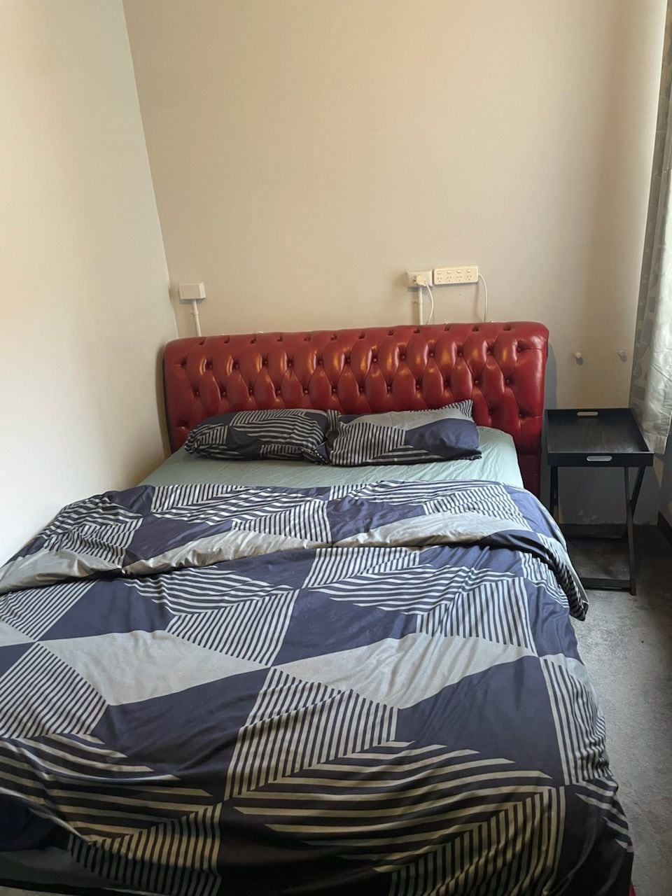 A bed with a red upholstered headboard, a striped bedspread, and two bedside tables.