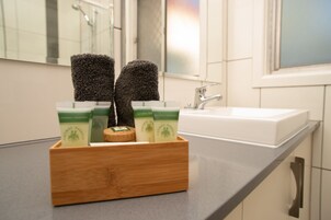 Un baño con un jabonera de madera que contiene dos esponjas negras y tres botellas de jabón esencial natural.