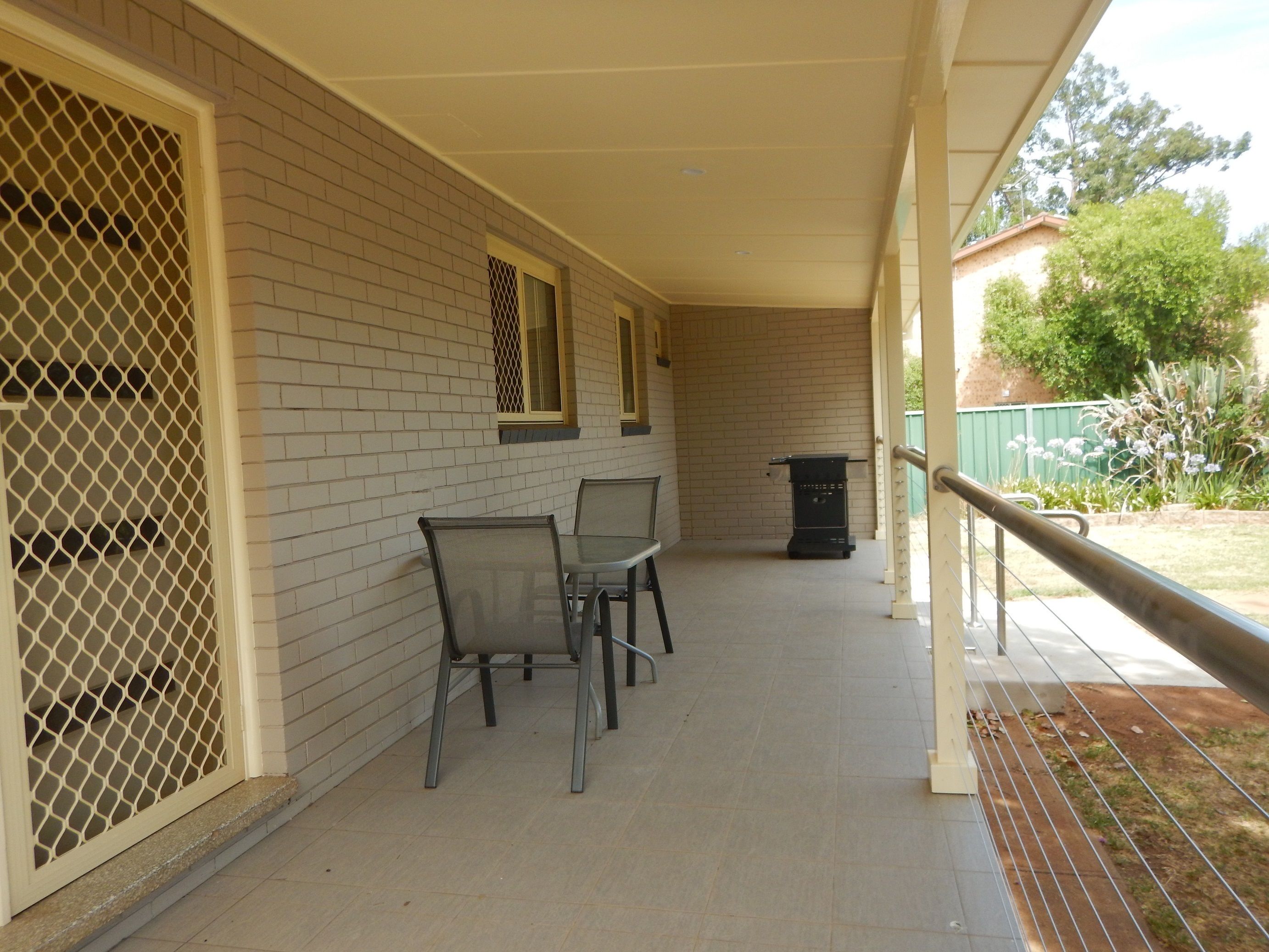 A covered outdoor area with a brick wall, two metal chairs, a small grill, and a trash can.