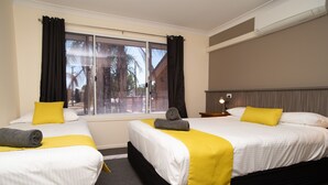A hotel room with two beds, each with a yellow and white bedspread, a grey towel on one bed, and a lamp on the nightstand. - Manera Heights Apartment Motel (Dubbo)