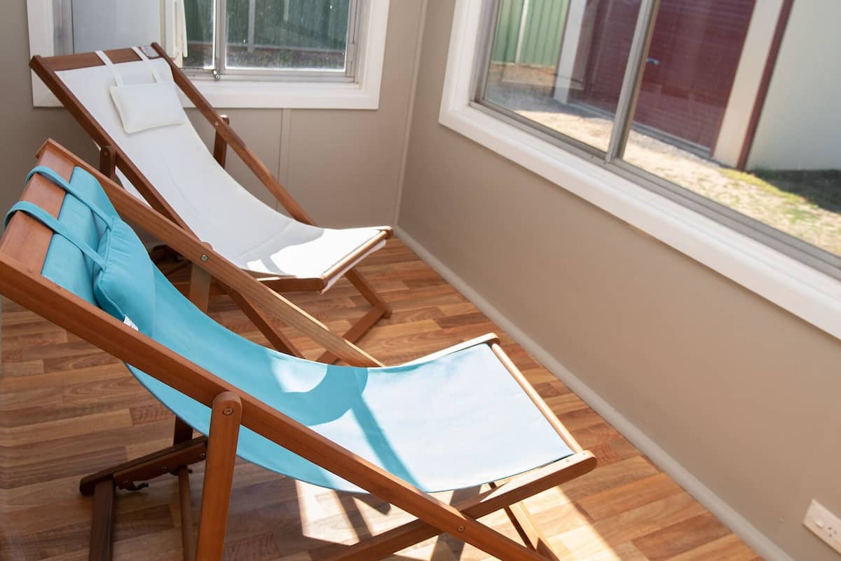 Una sala de estar con ventanales, tres sillones de madera y suelo de madera.