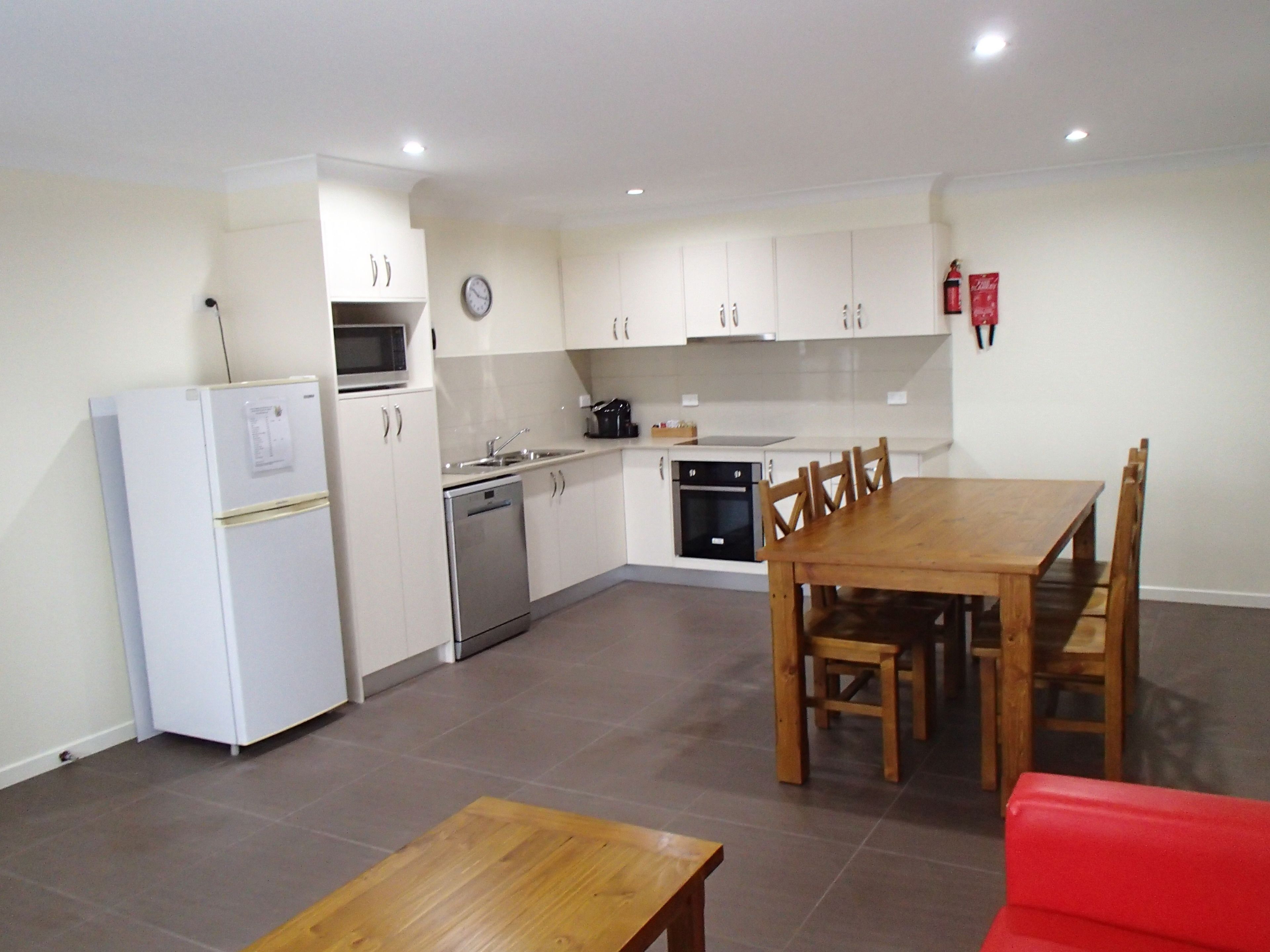 A compact kitchen with white cabinets, a microwave, a dishwasher, and a stove. There is a wooden dining table with chairs and a red sofa.