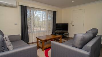 A living room with two grey sofas, a wooden coffee table, a flat-screen TV, and a large window with sheer curtains.