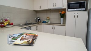 A kitchen with white cabinets, a microwave, a kettle, and a magazine on the counter. - Manera Heights Apartment Motel (Dubbo)