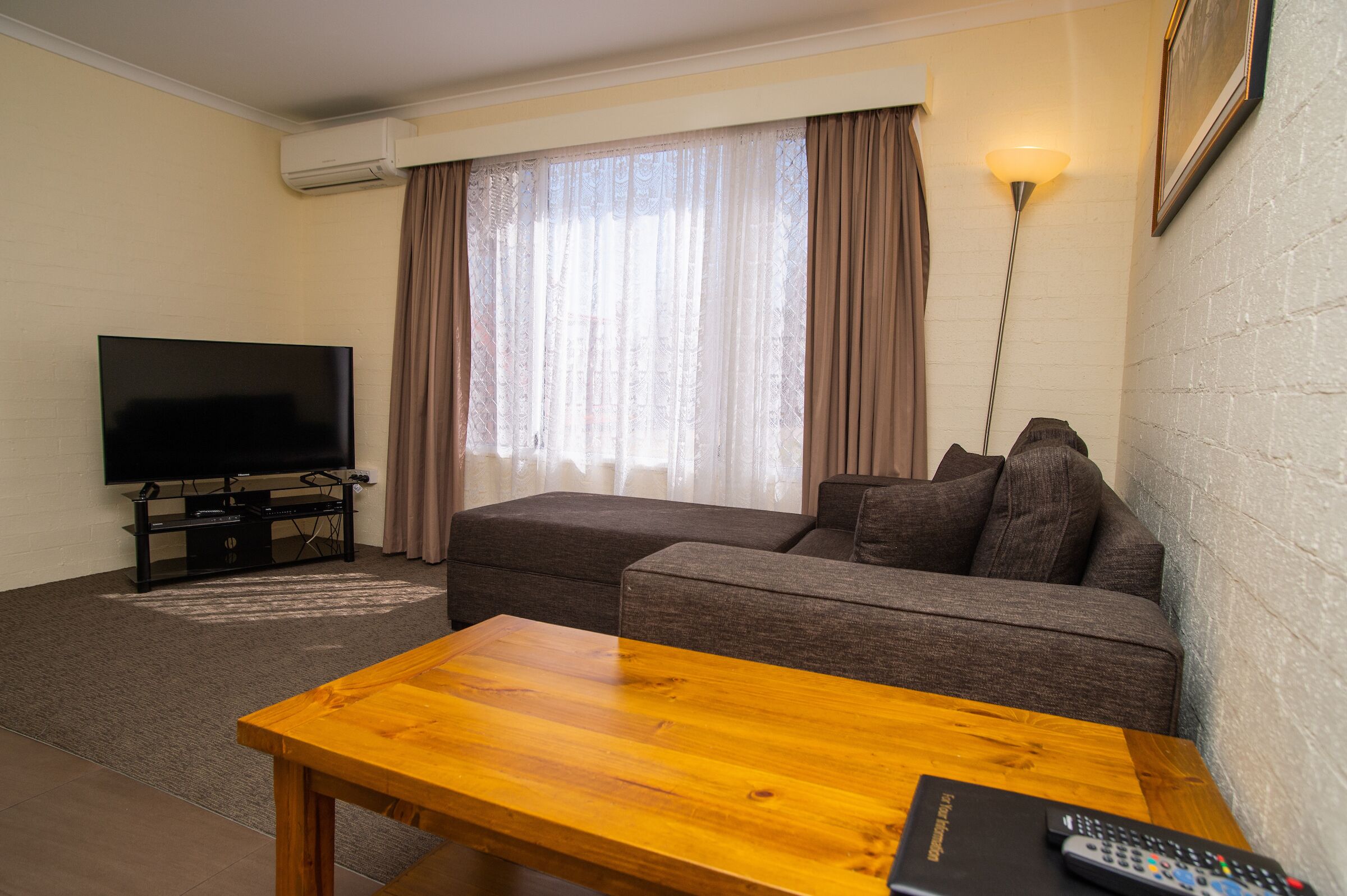 Una sala de estar con un televisor de pantalla plana, una mesa de centro de madera, un sofá y una lámpara.