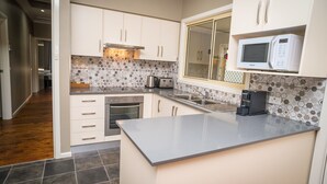 A modern kitchen with white cabinets, a built-in microwave, a coffee maker, and a patterned backsplash. - Manera Heights Apartment Motel (Dubbo)