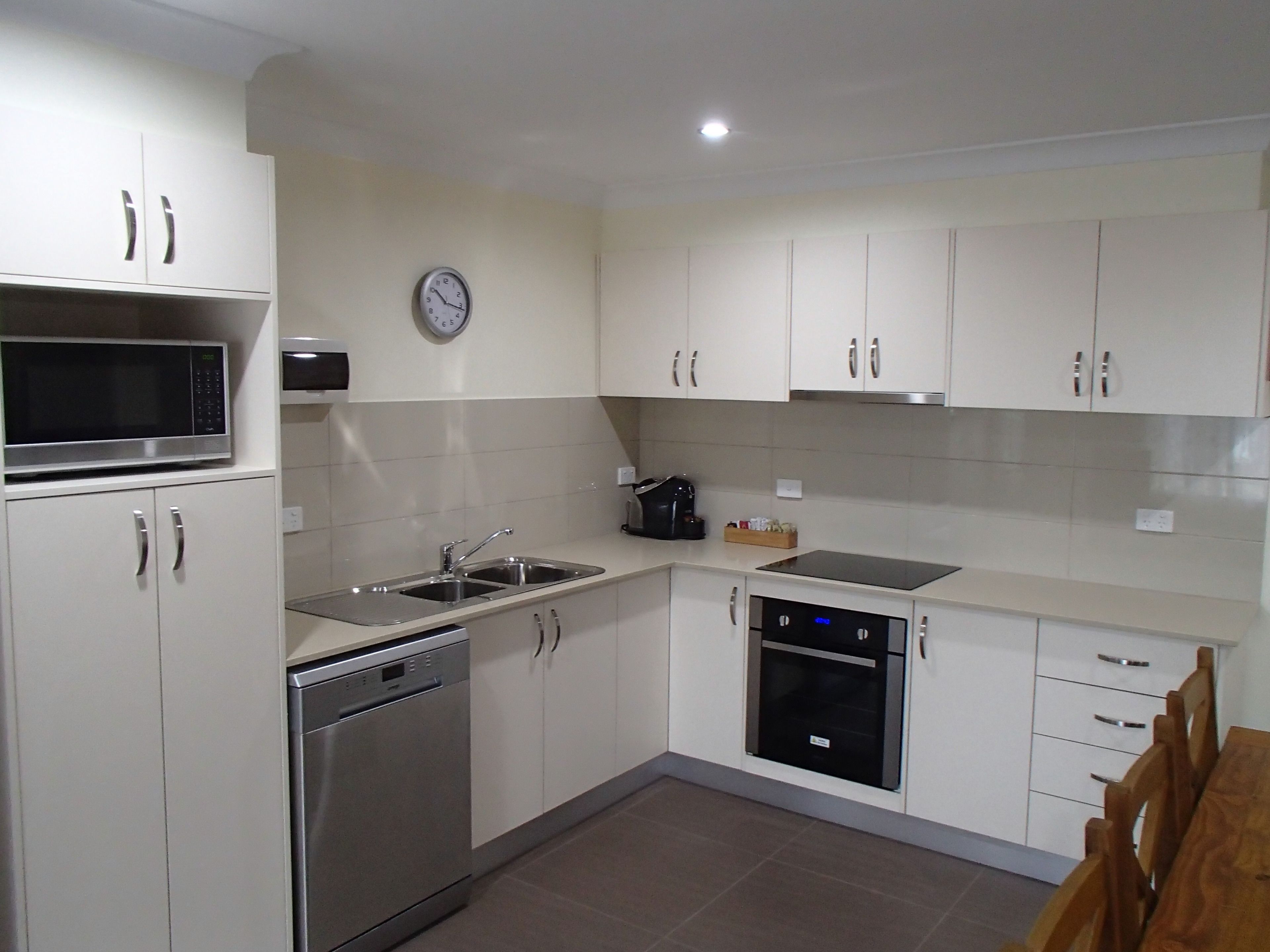 A modern kitchen with white cabinets, stainless steel appliances, and a clock on the wall.