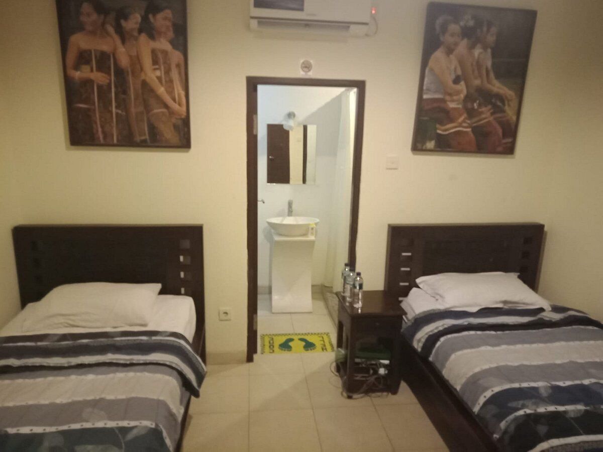 A hotel room with two single beds, a small bedside table with a lamp, a mirror, and a wall-mounted air conditioner.