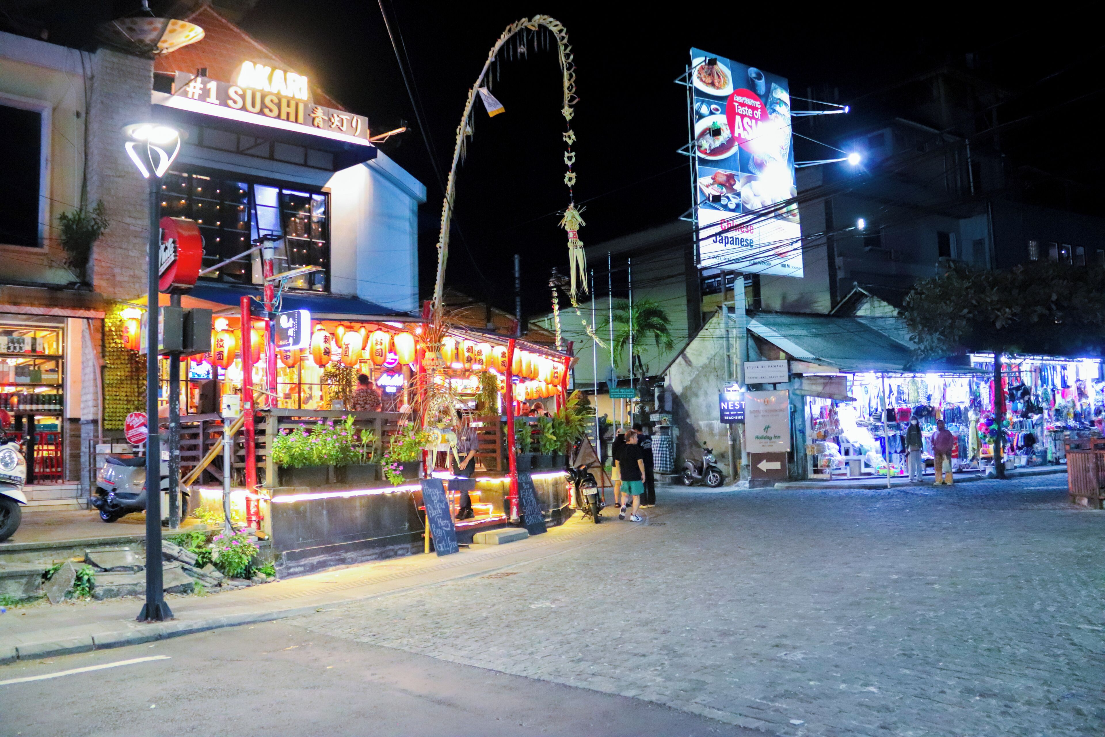 A sushi restaurant with a neon sign, outdoor seating, and a street view.