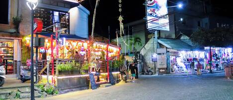 A sushi restaurant with a neon sign, outdoor seating, and a street view.