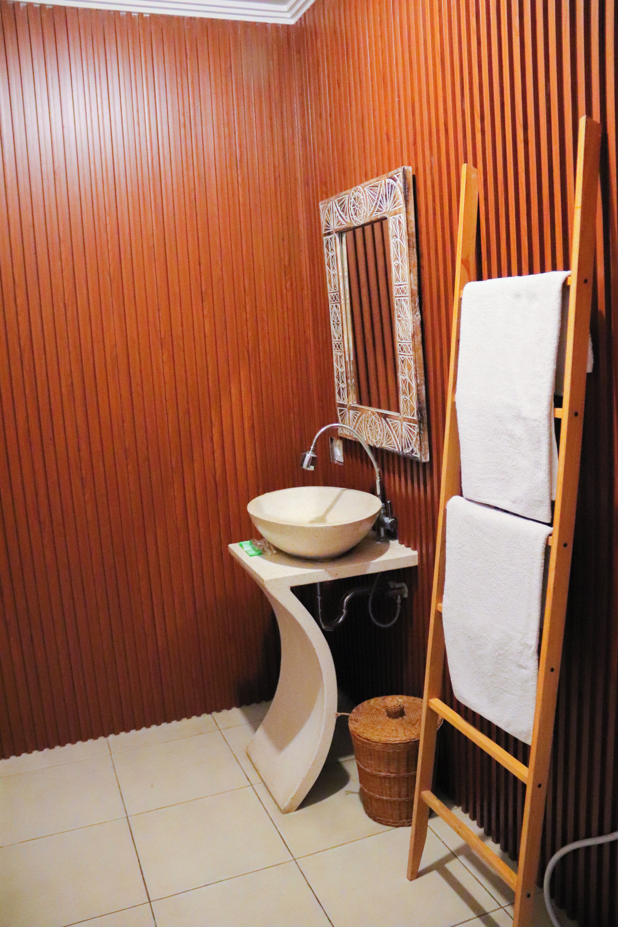 A bathroom with wooden paneling, a white sink, a mirror, and a wooden ladder with a towel.