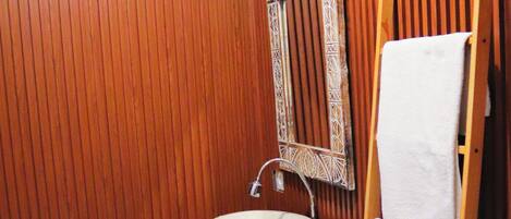 A bathroom with wooden paneling, a white sink, a mirror, and a wooden ladder with a towel.