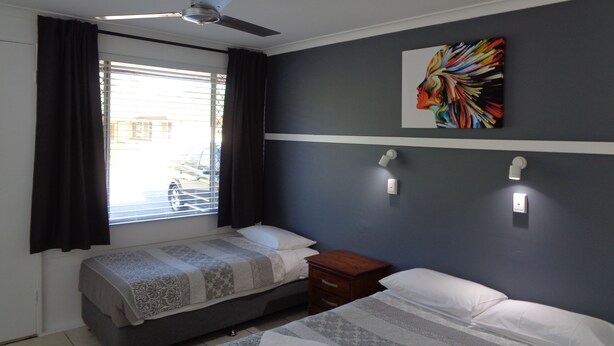 A bedroom with two beds, a ceiling fan, a window with curtains, and a wall-mounted light fixture. - Aspley Sunset Motel (Aspley)