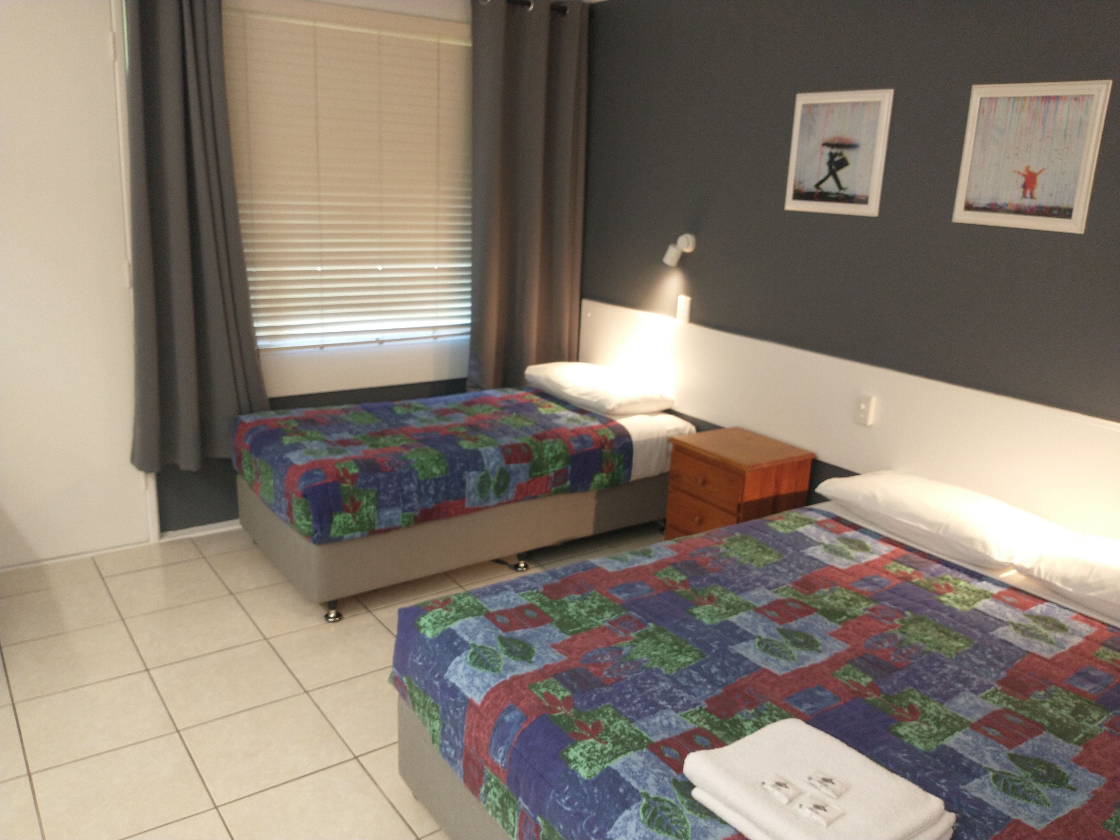 Una habitación de hotel con dos camas, una mesita de noche, una lámpara y dos cuadros en la pared.